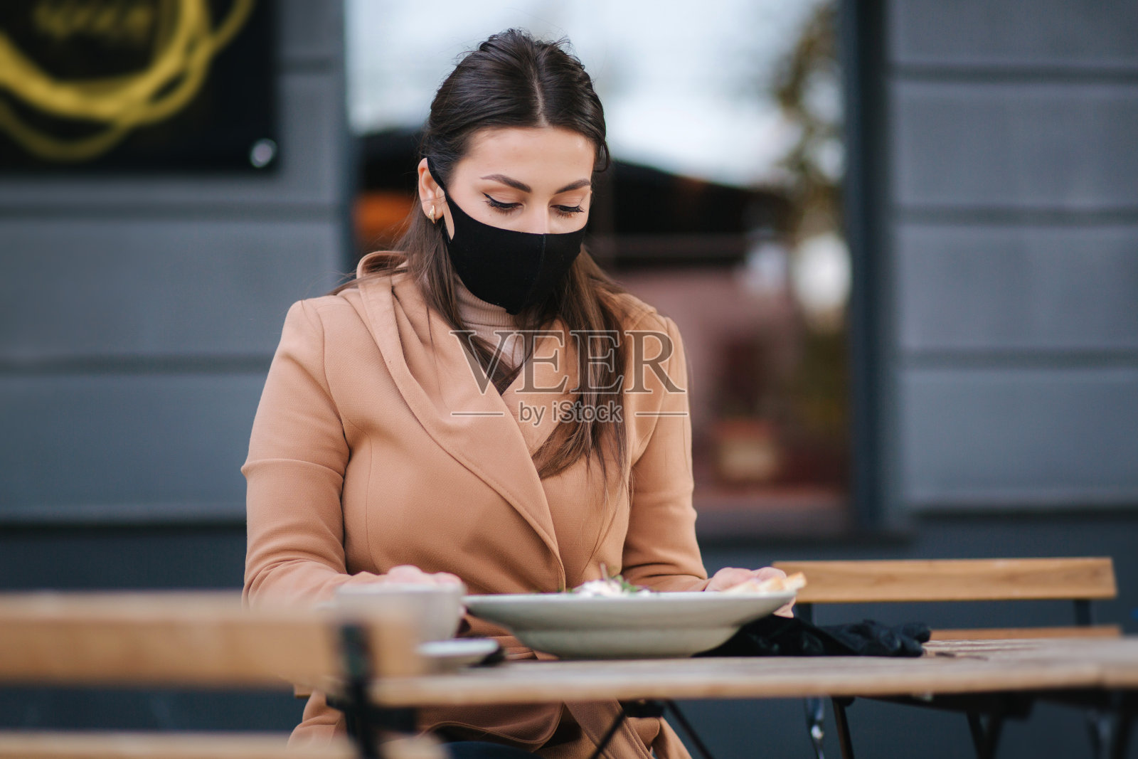 美丽的年轻女子在露天咖啡厅吃午餐。戴着黑色防护面具的女性。女人在吃饭时摘下口罩照片摄影图片