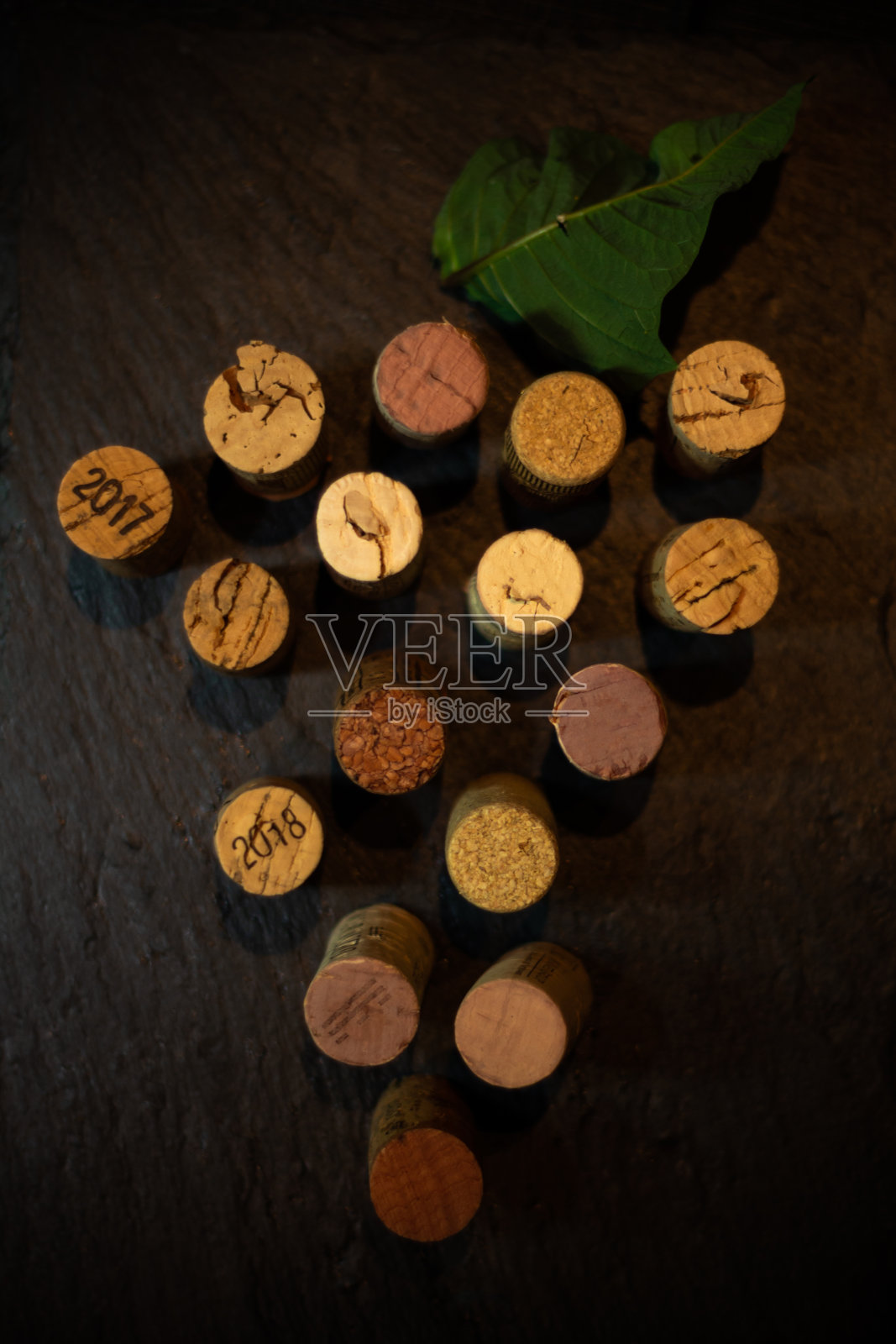 俯视图葡萄酒软木塞形成一串葡萄与一片葡萄叶子在石板与黑暗的背景照片摄影图片