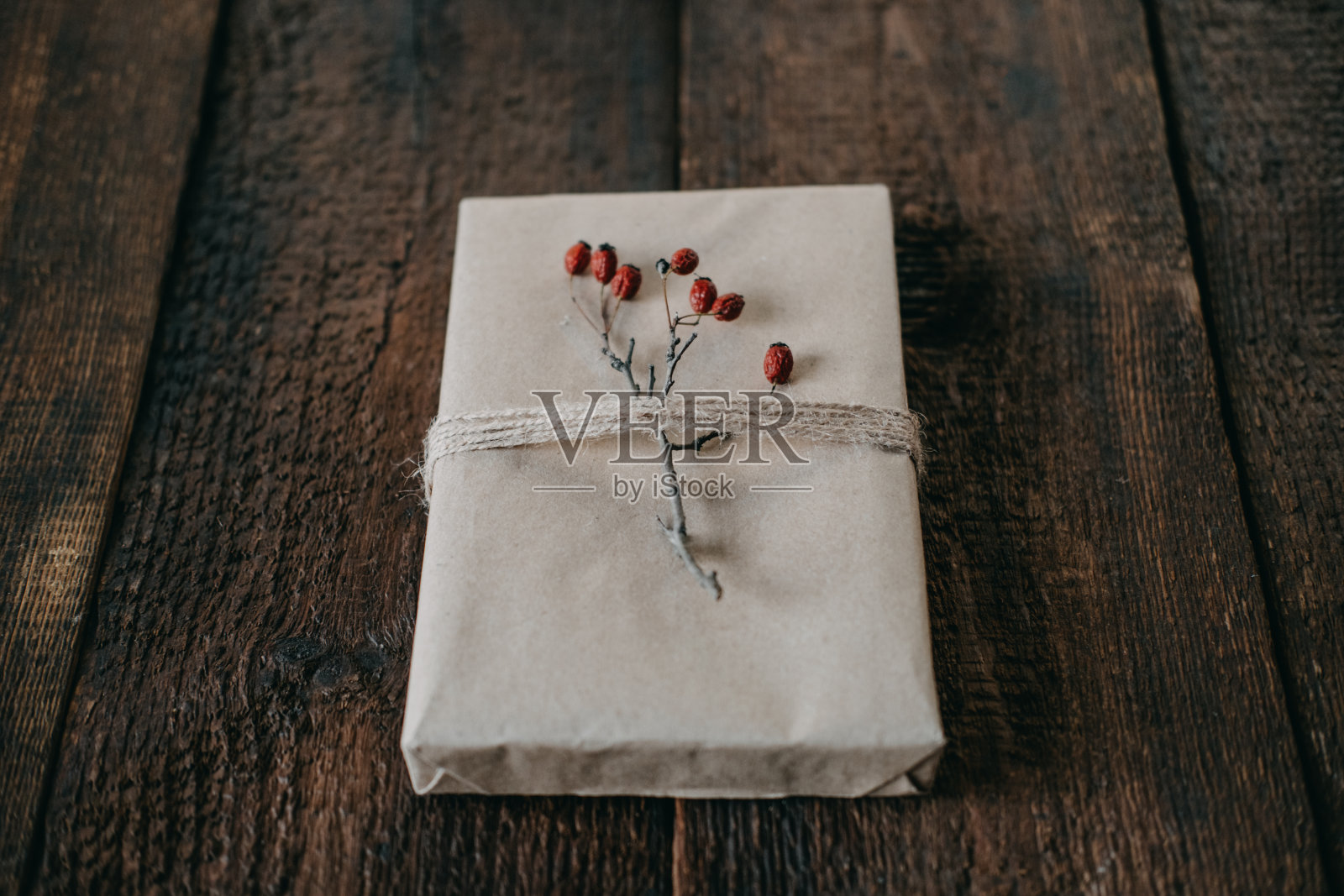 环保，可持续，零浪费的圣诞礼物包装牛皮纸与麻绳和浆果装饰。圣诞包装的礼物盒与自然装饰的木制背景照片摄影图片