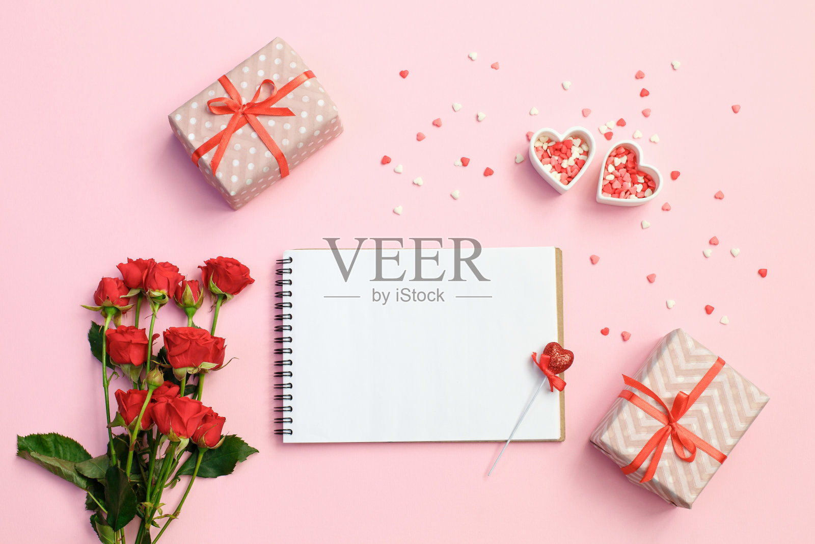打开空白笔记本与礼品盒，鲜花和心在粉红色的背景。情人节的背景。照片摄影图片