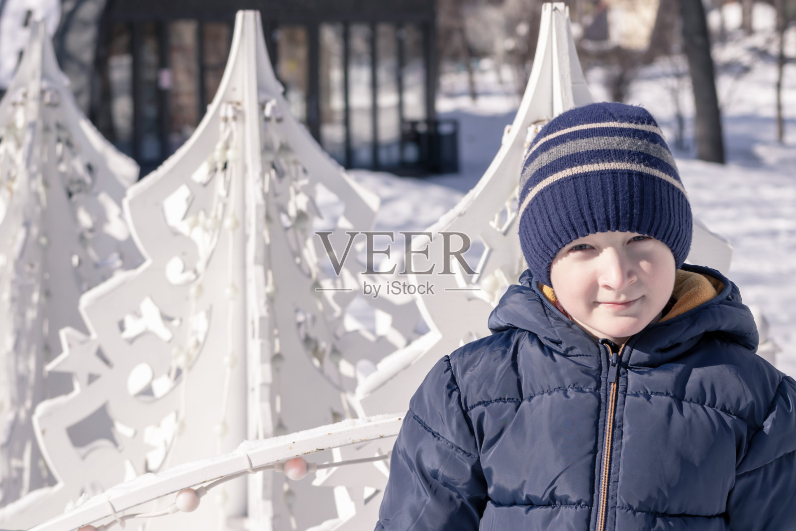 一个男孩站在户外白色的圣诞装饰品前，阳光明媚的冬日和雪景，复制空间照片摄影图片