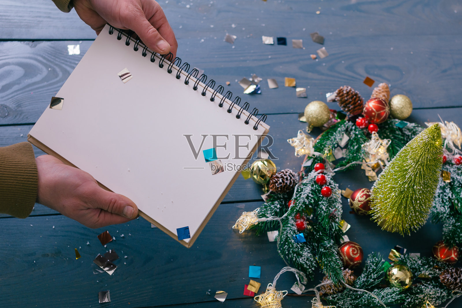 一个男人拿着一个记事本，放在一个装饰好的木桌上。新年和圣诞节的节日作文。照片摄影图片