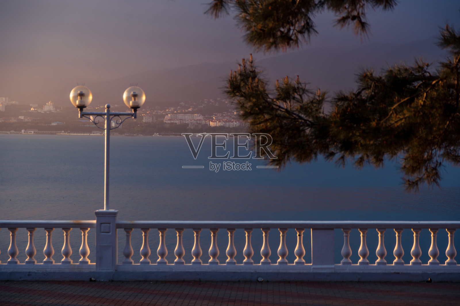 落日非常美丽，对比突出了格伦季克度假胜地的堤岸栏杆。在前景中是一根松枝。背景是大海和黑暗的群山照片摄影图片