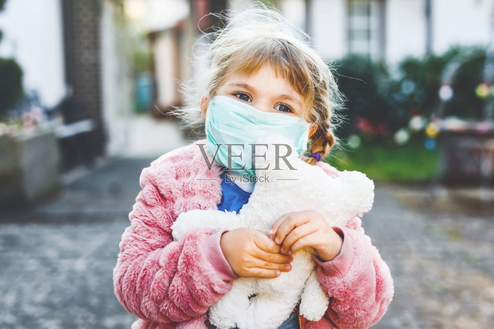 小女孩戴着医用口罩，以保护自己免受冠状病毒隔离疾病的侵袭。可爱的孩子使用防护设备对抗covid - 19和持有熊玩具。照片摄影图片