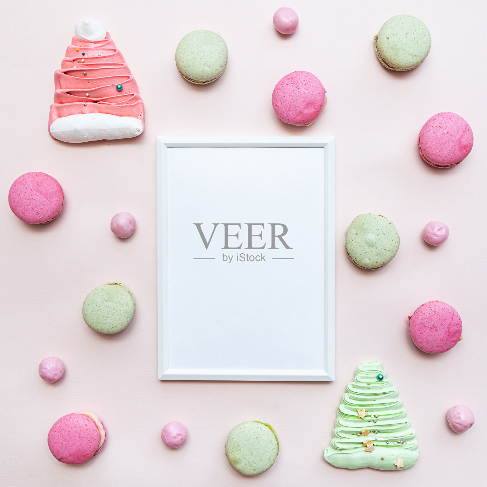 白色空白相框模型与各种糖果，杏仁蛋白饼干，蛋白酥和糖果。平躺在粉红色的桌子上照片摄影图片