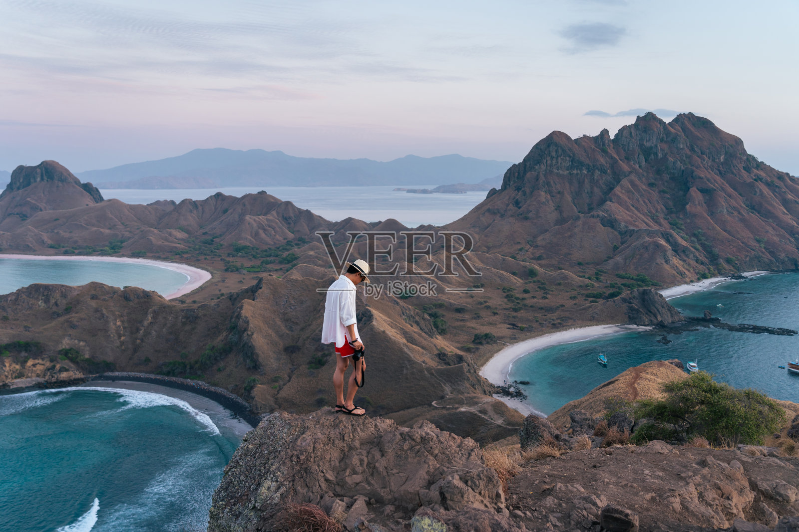 在印度尼西亚弗洛雷斯岛的科莫多国家公园里，一个年轻的亚洲旅行者拿着相机站在帕达岛的顶部照片摄影图片