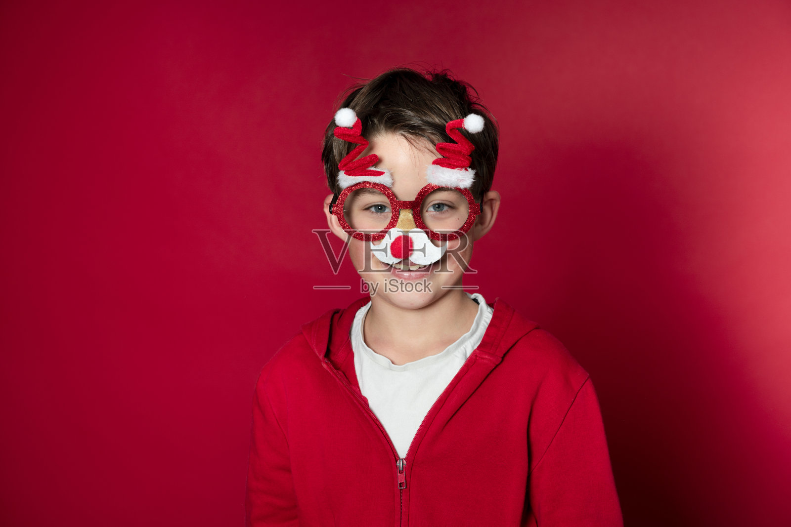 小男孩在红色背景下戴着有趣的圣诞眼镜庆祝圣诞节照片摄影图片