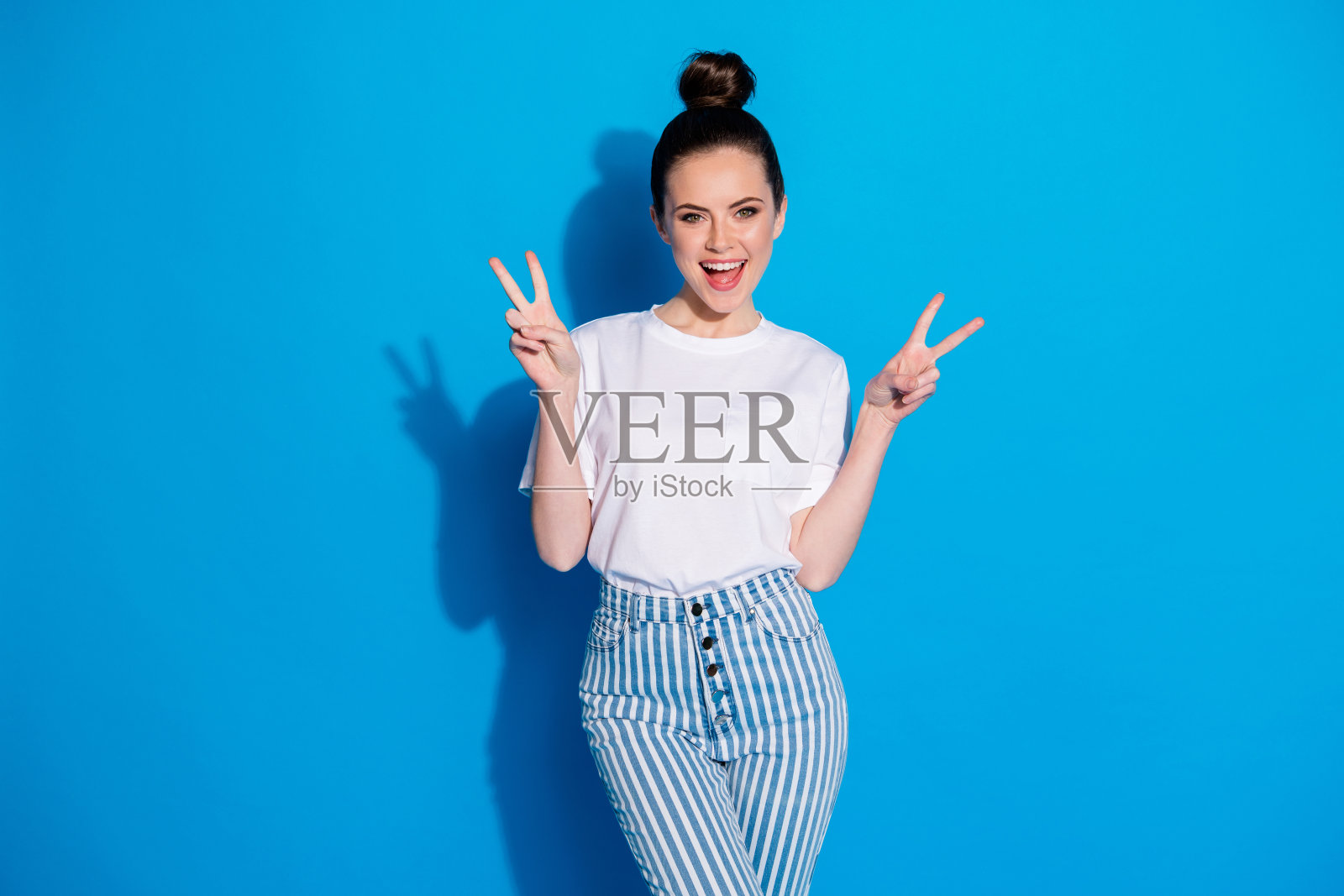 她的肖像，她很好，有吸引力，可爱，漂亮，迷人，高兴，愉快，快乐的女孩显示v-sign，有乐趣的春天孤立在明亮，生动的，充满活力的蓝色背景照片摄影图片