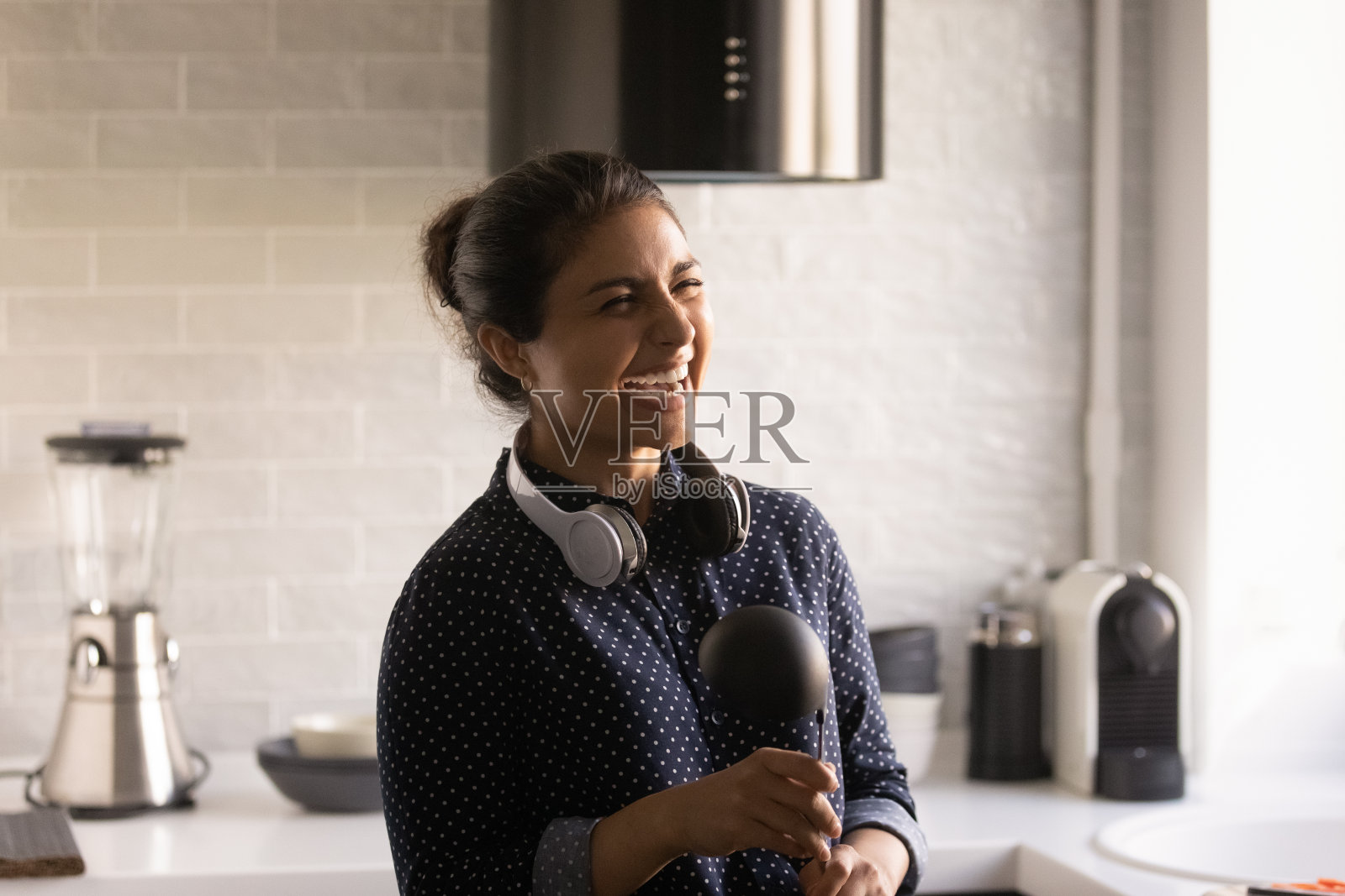 笑着的印度女人戴着无线耳机在厨房唱卡拉ok照片摄影图片