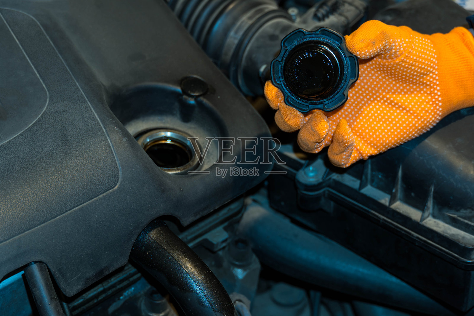 这是一只戴着橙色手套的手拿着汽车发动机油塞的图像。照片摄影图片