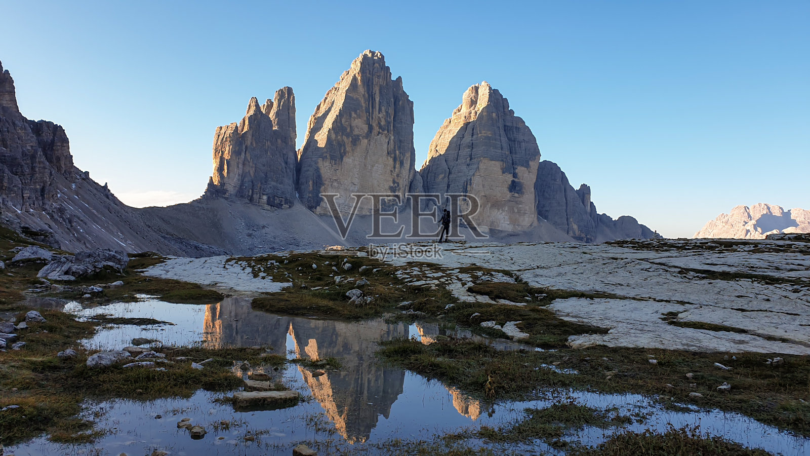 一名男子正在欣赏意大利Dolomites地区的Drei Zinnen山。群山倒映在小桨里。荒凉和原始的景观。清晨。黎明照片摄影图片