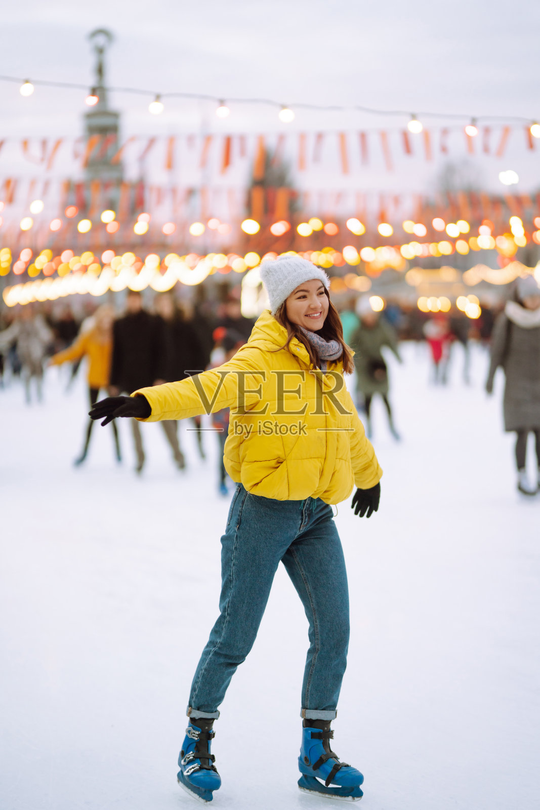 快乐的女人在节日圣诞集市的城市广场的冰场上滑冰。照片摄影图片