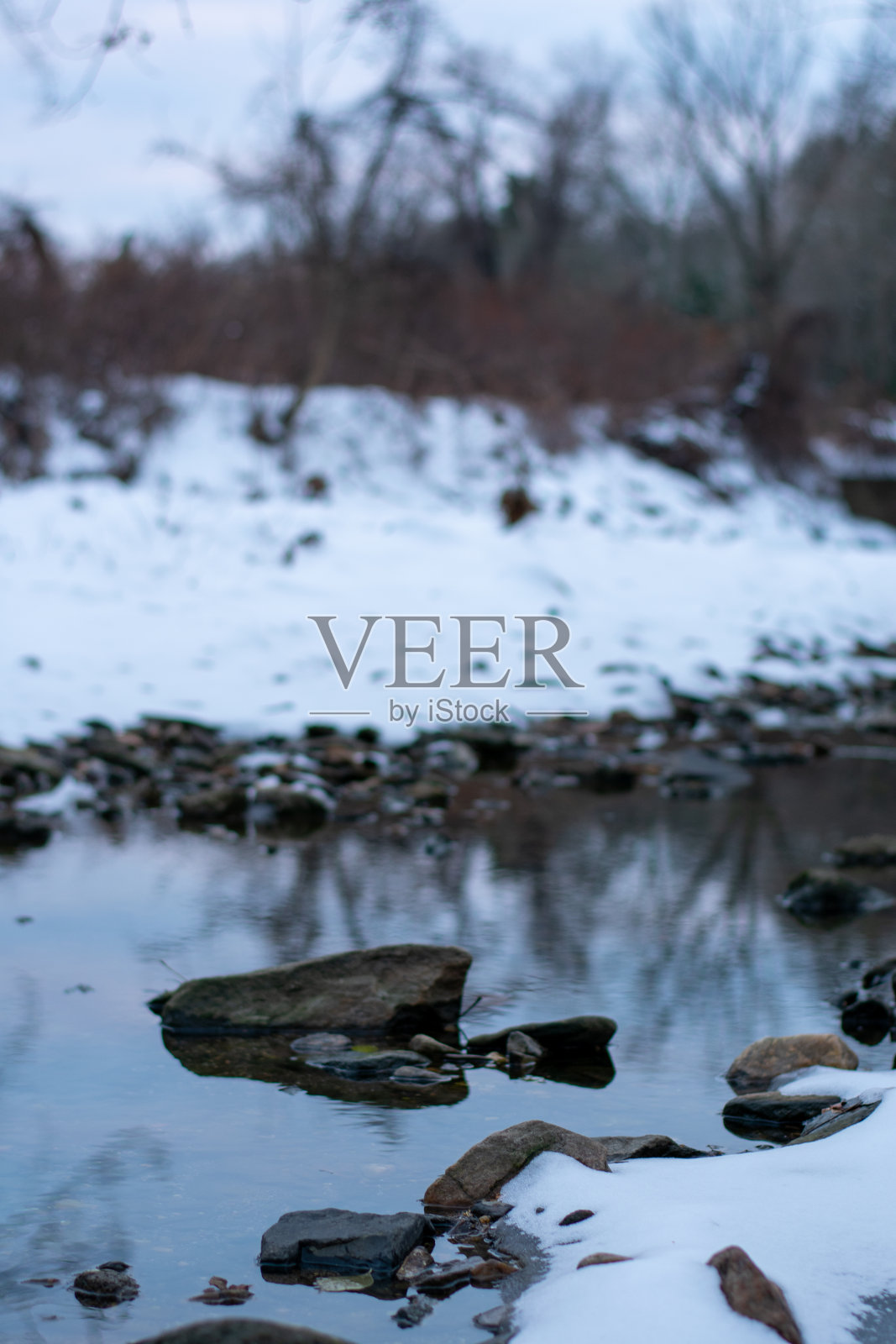 白雪覆盖的森林里一条小河里的一块石头照片摄影图片