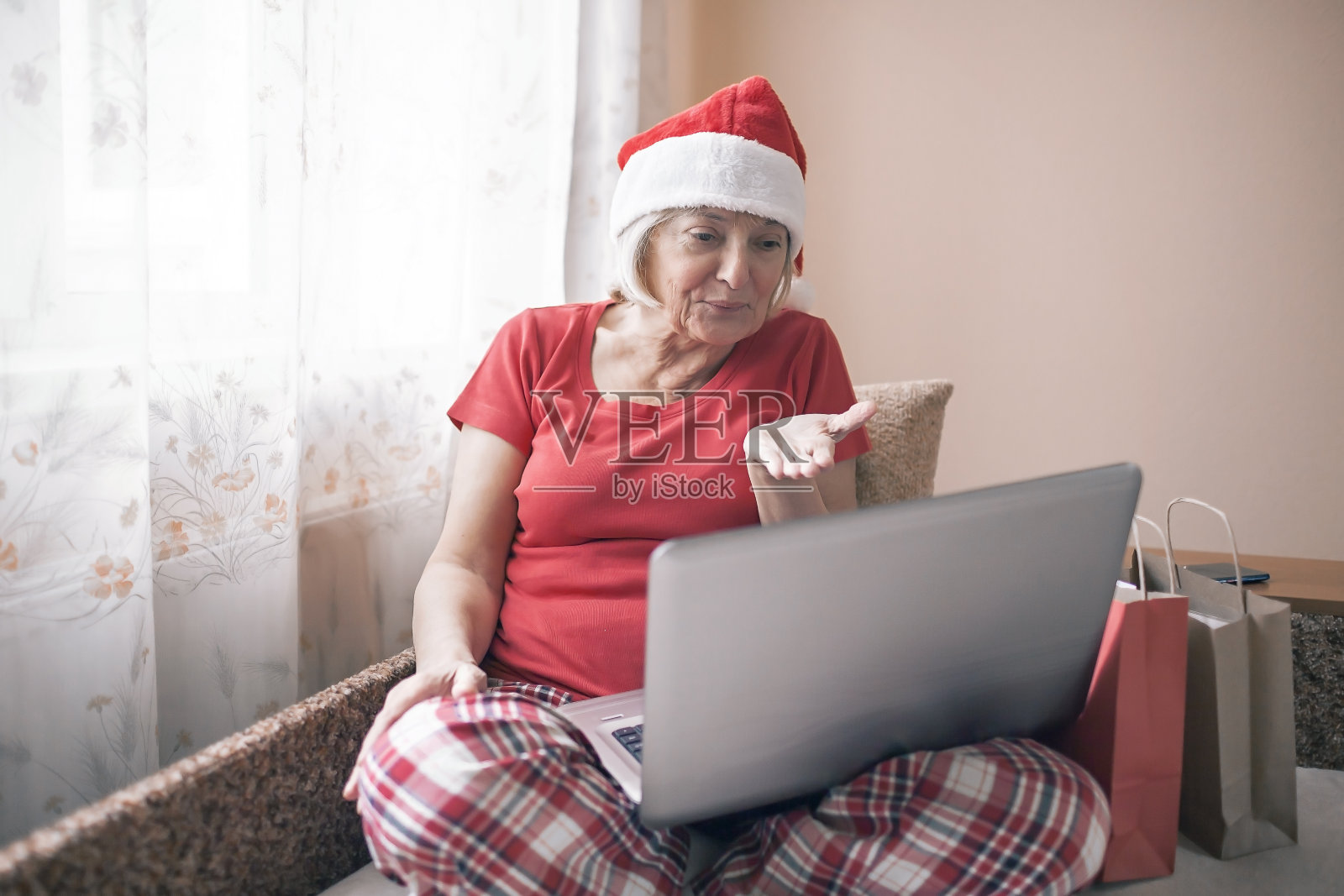 安全的在线圣诞节。老妇人戴着圣诞老人的帽子在网上送礼物照片摄影图片