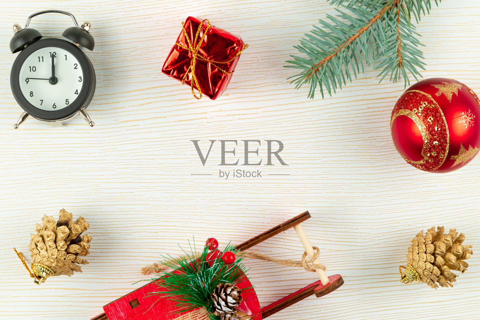 闹钟、圣诞老人雪橇、白木背景上的金松果和圣诞球照片摄影图片