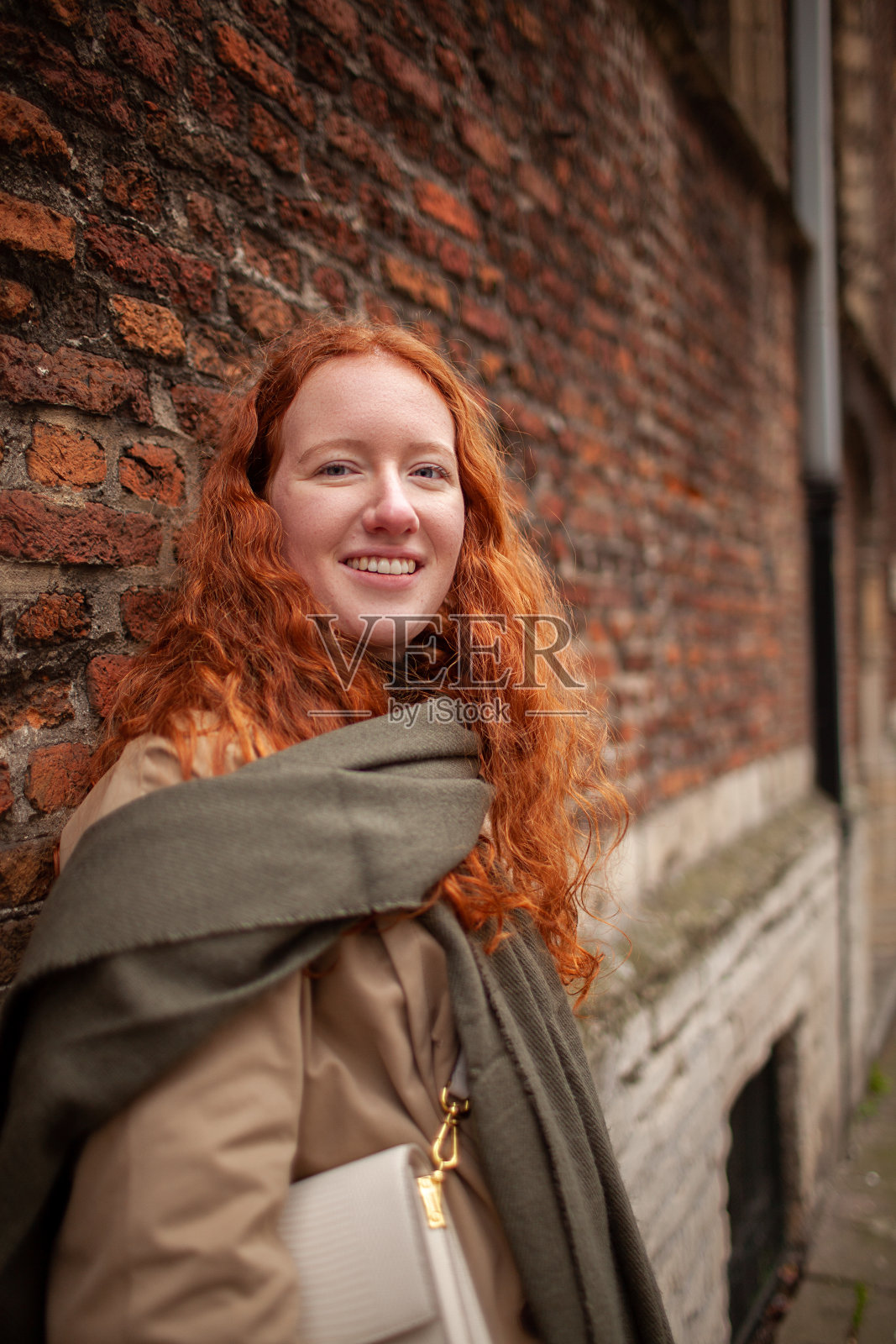 街头人像：长卷发红发少女靠在红砖墙上照片摄影图片