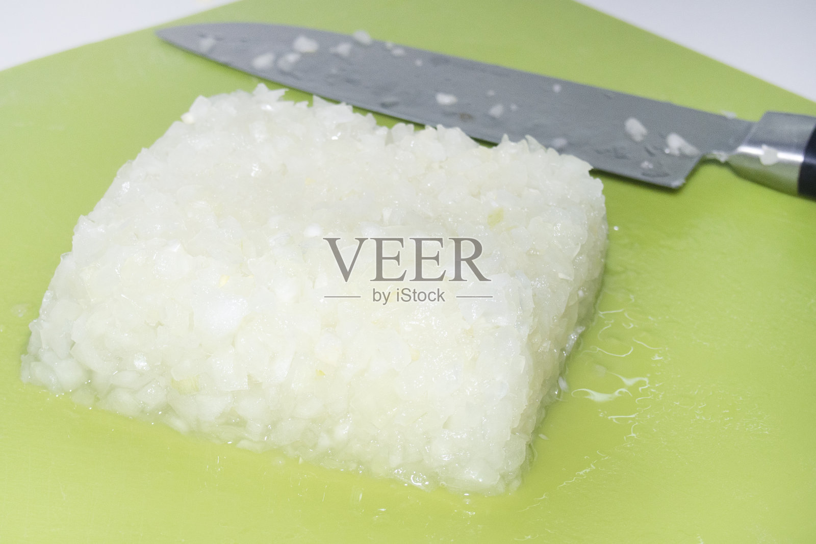 切碎的新鲜洋葱放在绿板上，旁边放一把刀照片摄影图片