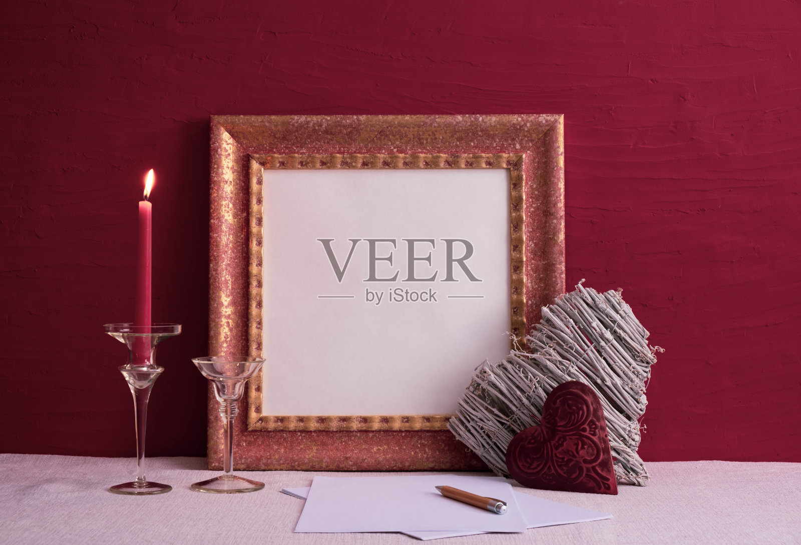 一条长腿上的烛台上点着一支蜡烛，两个心形的装饰品，桌子上一个红色背景上的旧相框照片摄影图片