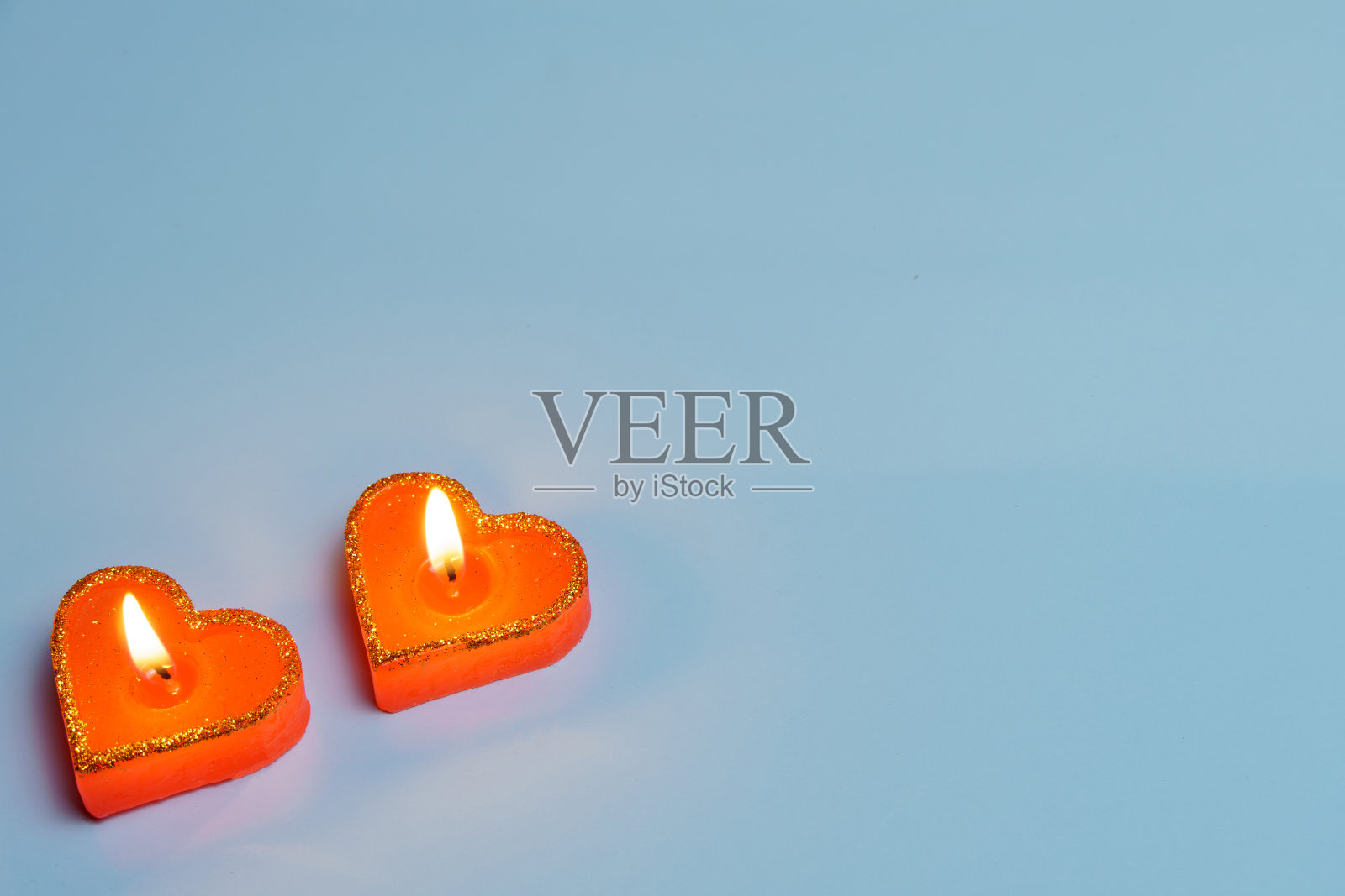 在蓝色的背景上，两支燃烧着的红色心型蜡烛——爱的象征。情人节。照片摄影图片