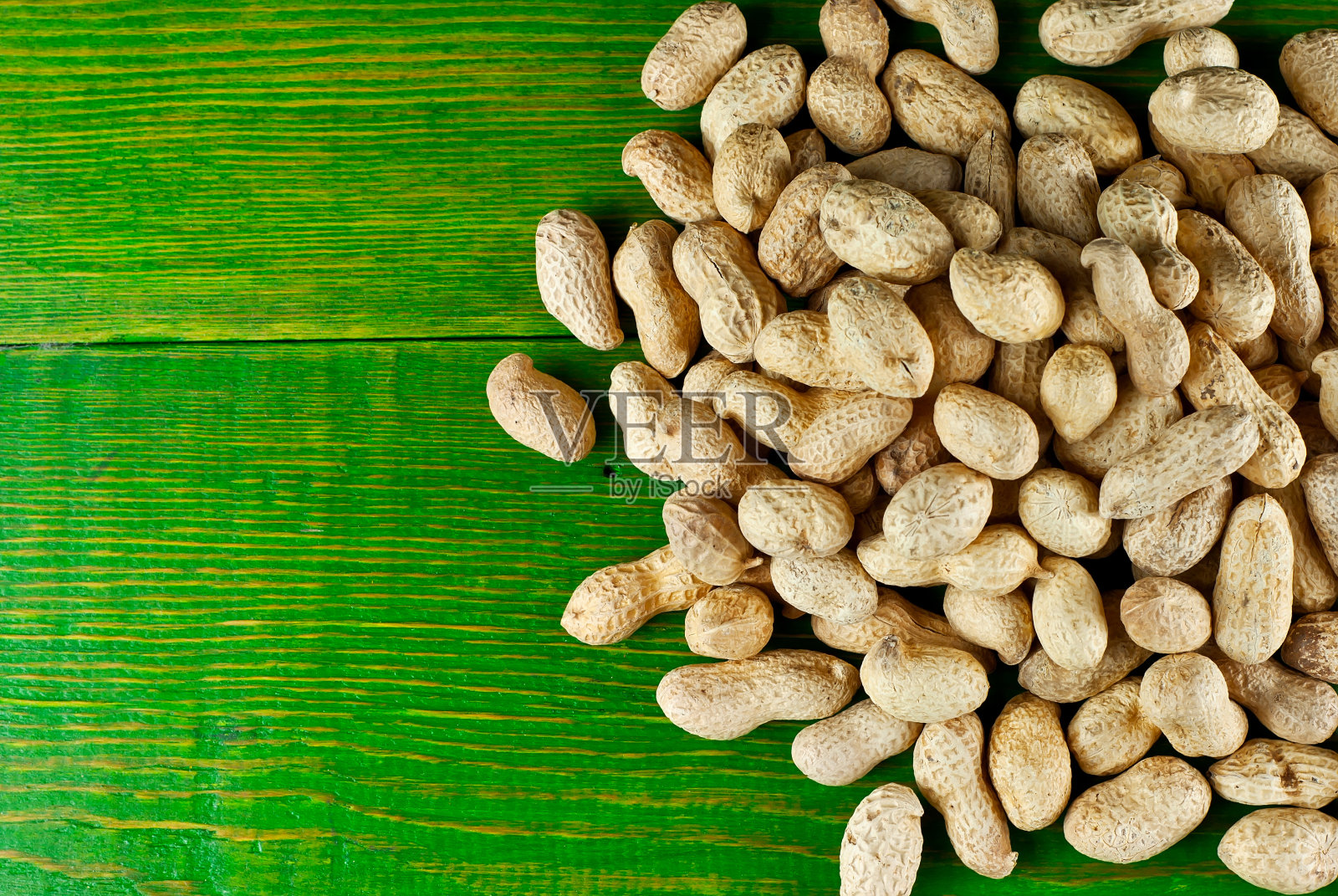 绿板上的带壳花生。旧木头桌子上坚果的纹理。很多坚果堆在一起。放置文本和复制空间附近的种子。照片摄影图片