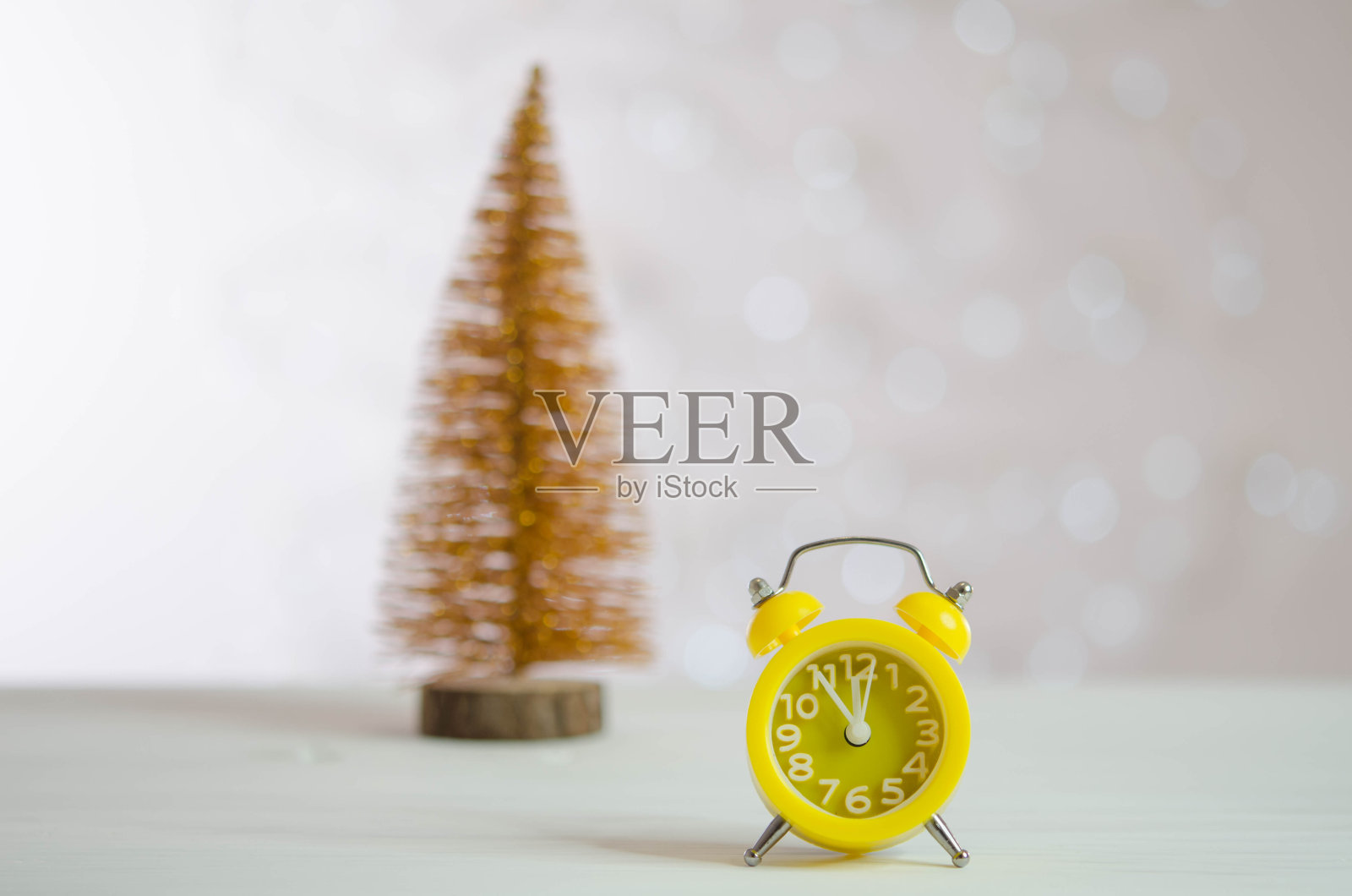 黄色的闹钟和金色的圣诞树在桌子上。照片摄影图片