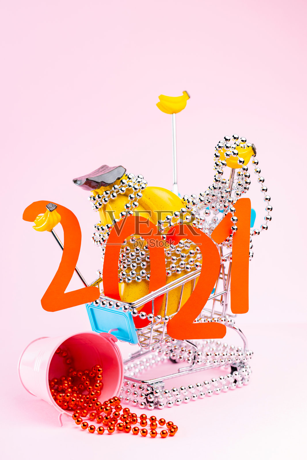 购物车里的圣诞树装饰品，以粉色为背景。红色圣诞树和购物车上的2021字。假日购物的概念照片摄影图片