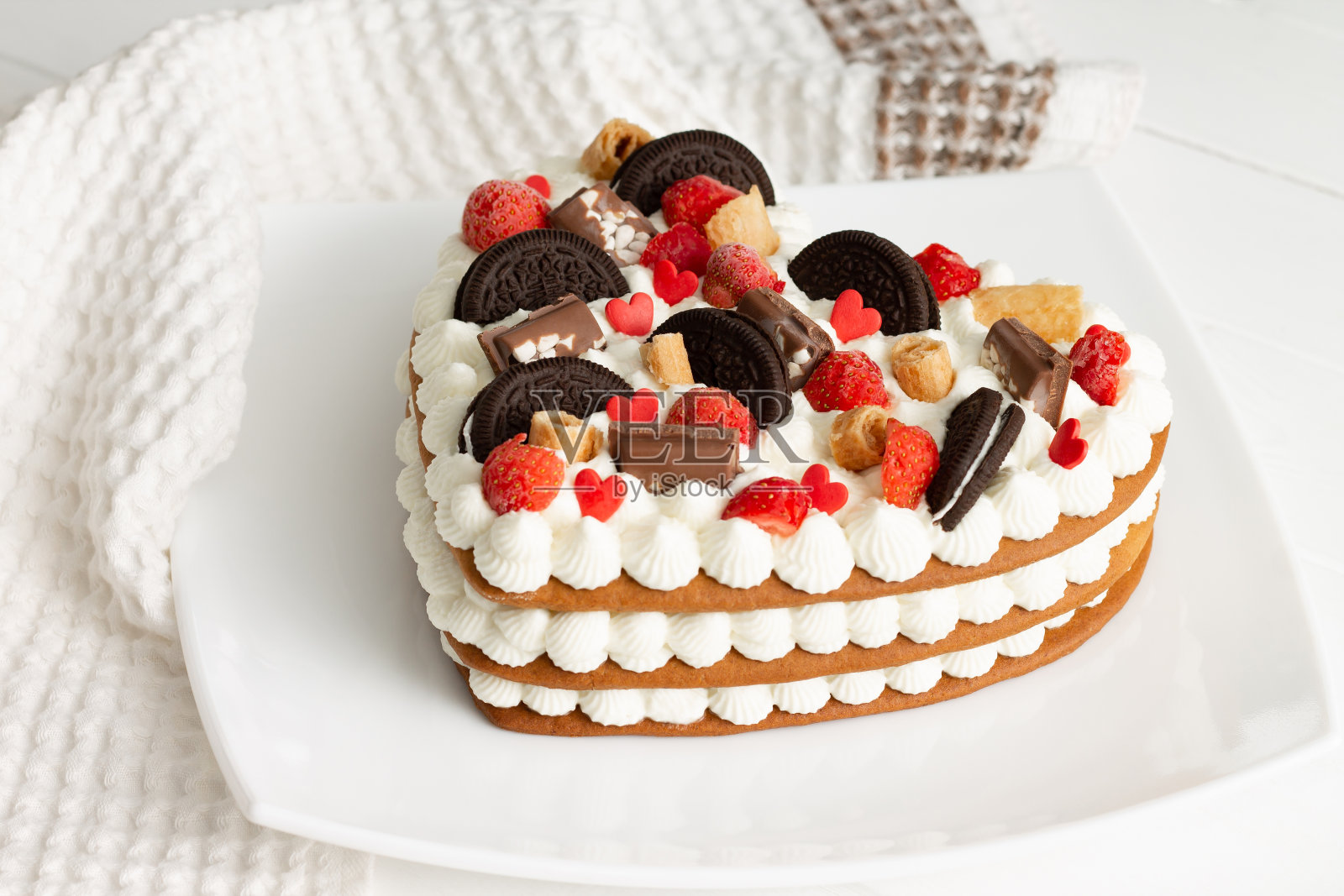 用乳清干酪和鲜奶油做成的心形蛋糕，用巧克力、华夫饼、饼干和草莓装饰照片摄影图片