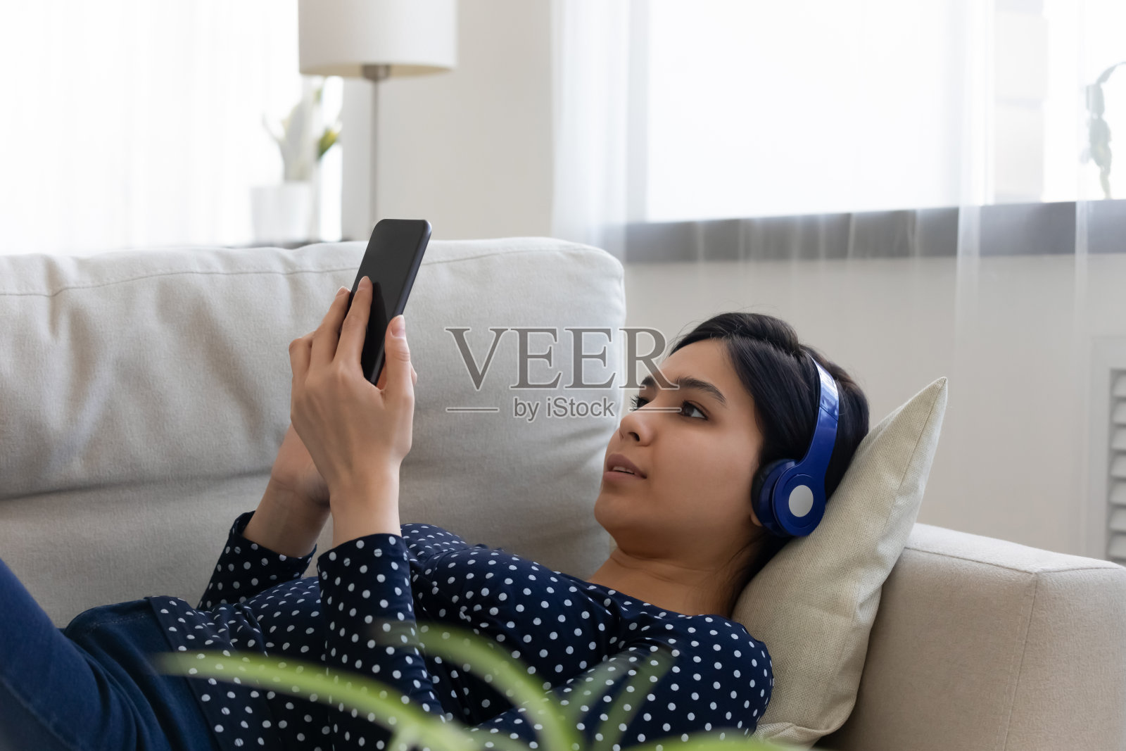 放松的亚洲女人戴着耳机使用智能手机观看视频照片摄影图片