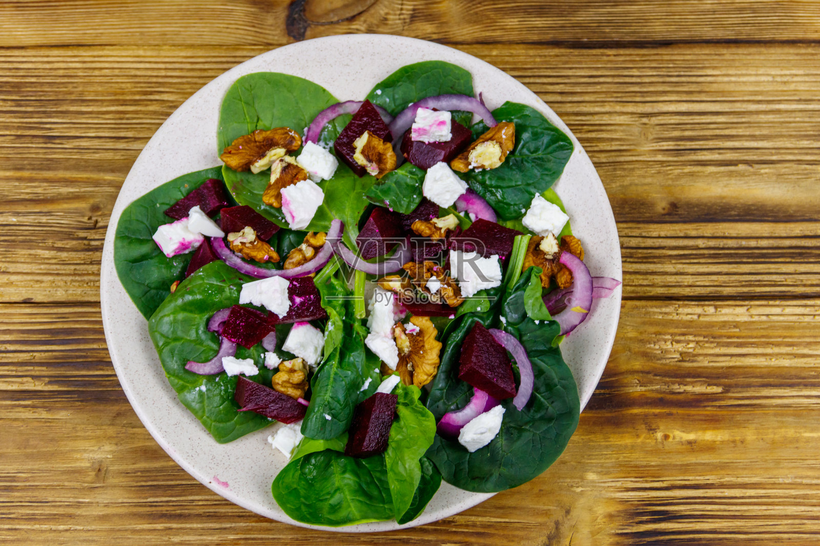 美味的菠菜沙拉配煮甜菜根，羊乳酪，核桃和红洋葱在木桌上。前视图。健康的素食照片摄影图片