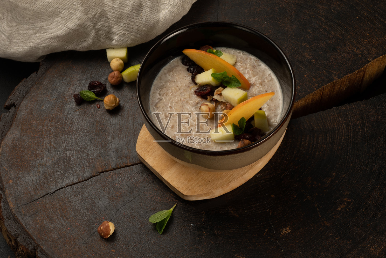 加水果、坚果和干果的牛奶燕麦粥。美味健康的早餐盛在一个很深的陶瓷碗里。照片摄影图片