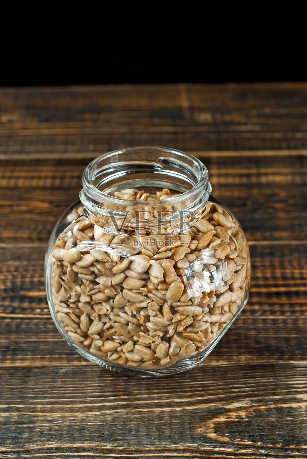葵花籽在玻璃透明的罐子里。破旧的木板上的坚果。罐子放在一张棕色的木桌上。照片摄影图片
