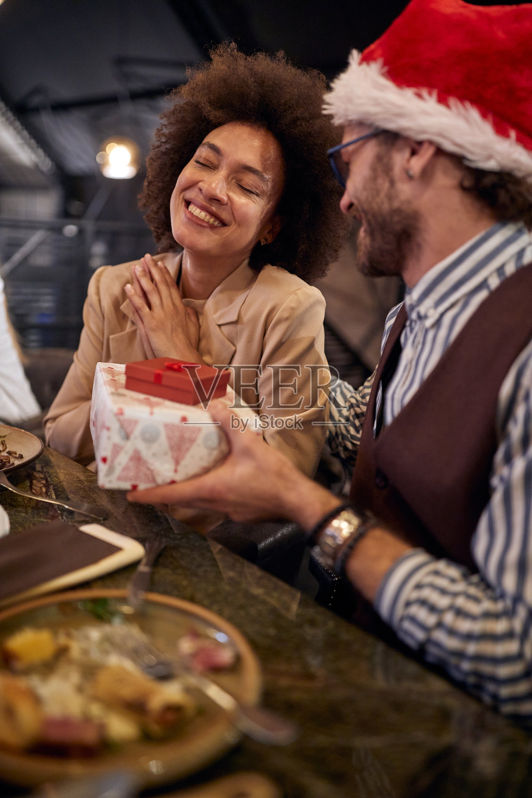 一位女同事在餐厅吃公司晚餐时收到男同事的新年礼物，她惊讶不已。一起，新年，一起庆祝照片摄影图片