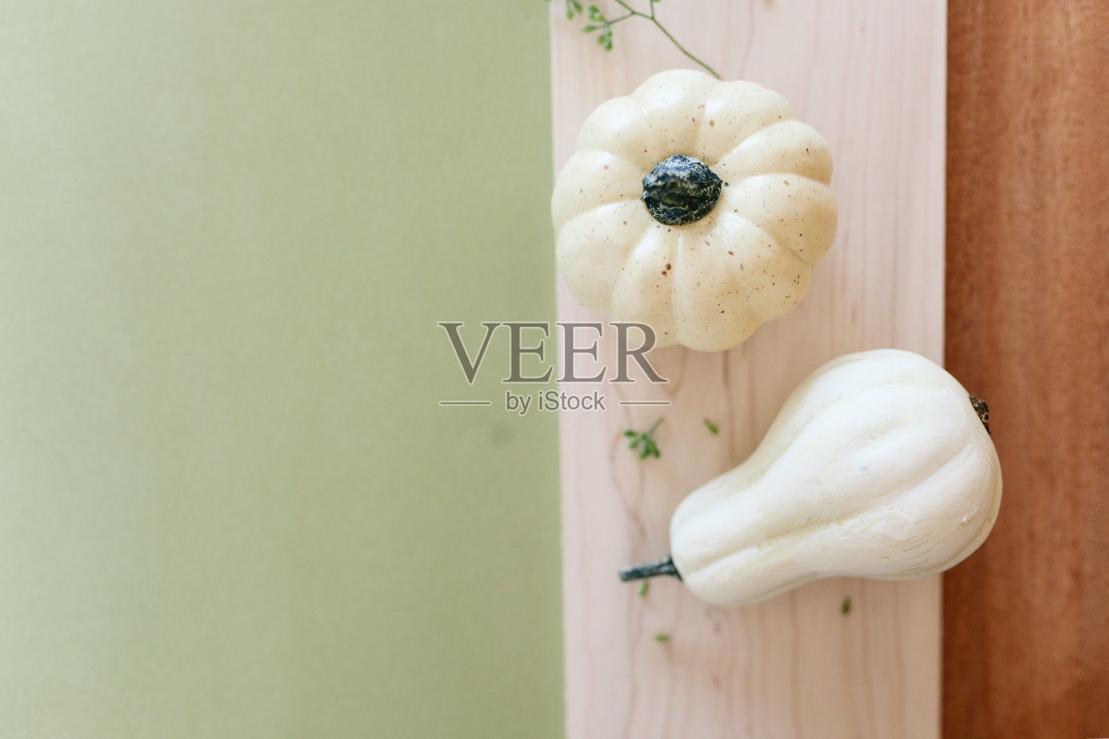 木制砧板上放着两个白色的小南瓜，背景是鼠尾草绿色照片摄影图片