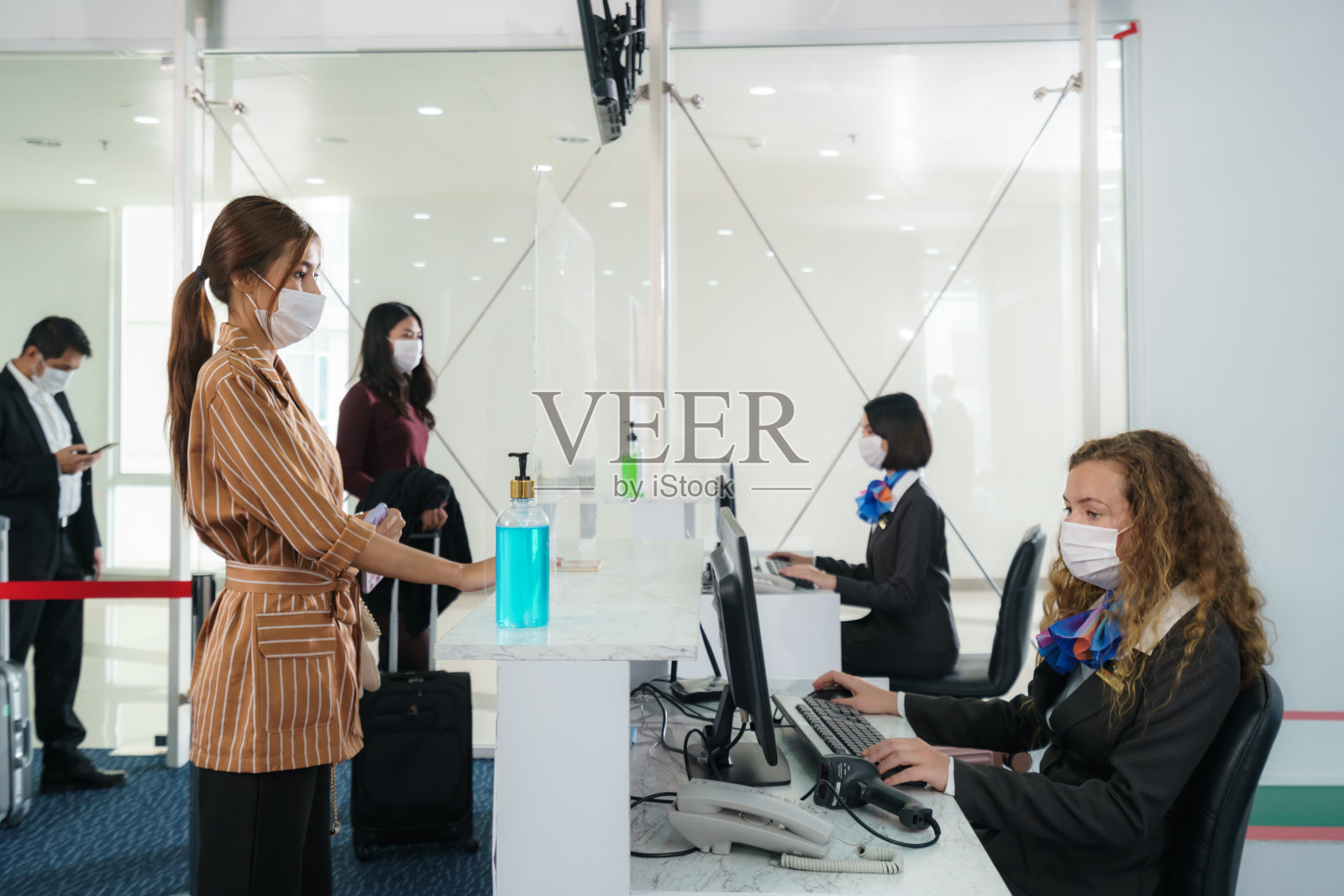 一名佩戴口罩的女乘客正在机场柜台通过丙烯酸屏障办理登机手续，以预防新冠肺炎或新冠肺炎疫情照片摄影图片