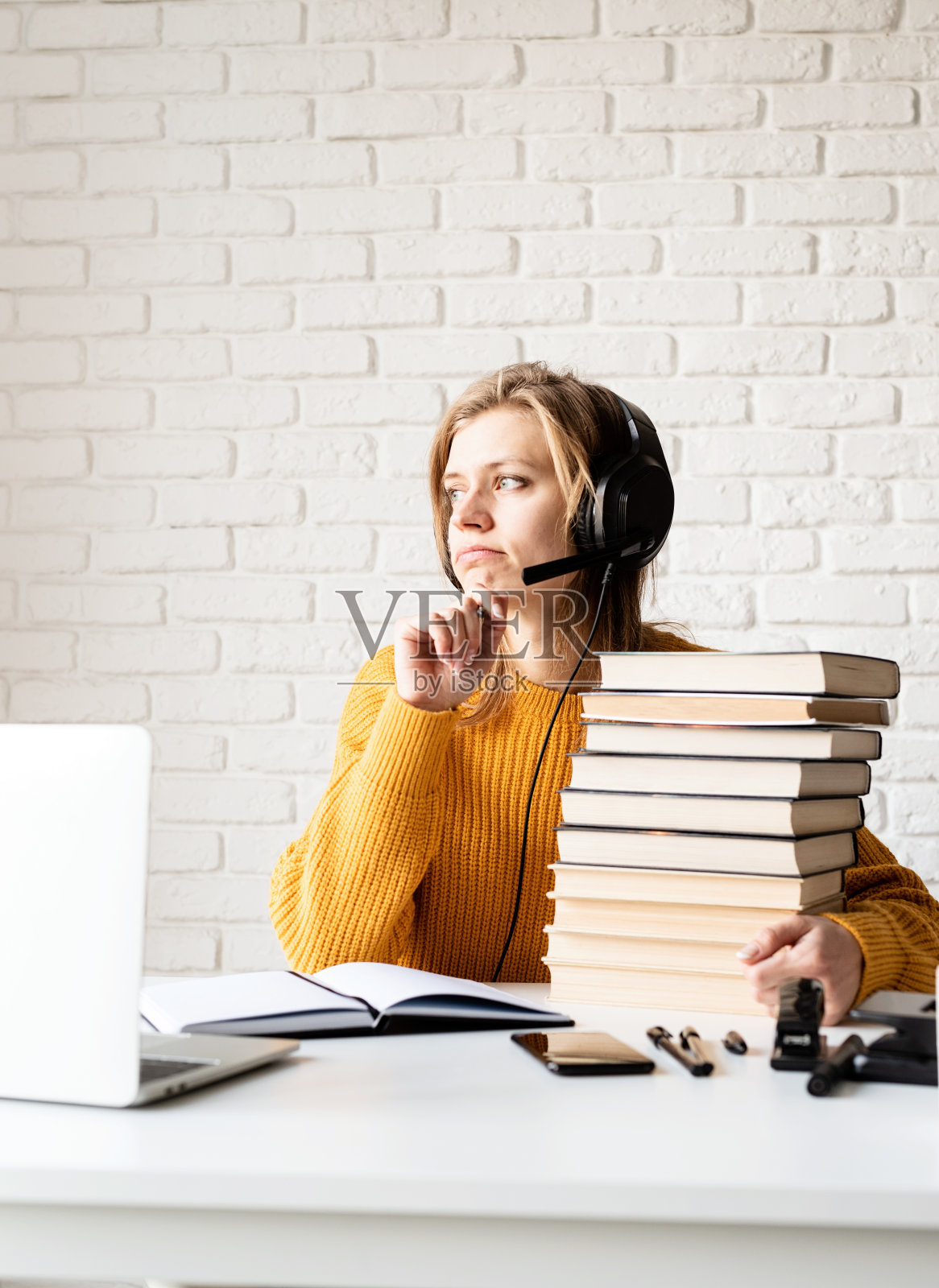 戴着黑色耳机微笑的年轻女子使用笔记本电脑在线学习，在笔记本上写字照片摄影图片