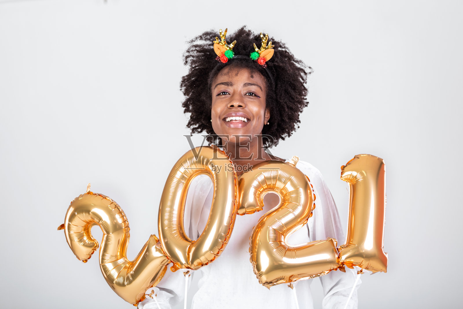 漂亮的黑色派对女孩，卷发和节日服装在工作室背景上摆姿势，手里拿着数字2021的金色气球，新年快乐的概念照片摄影图片