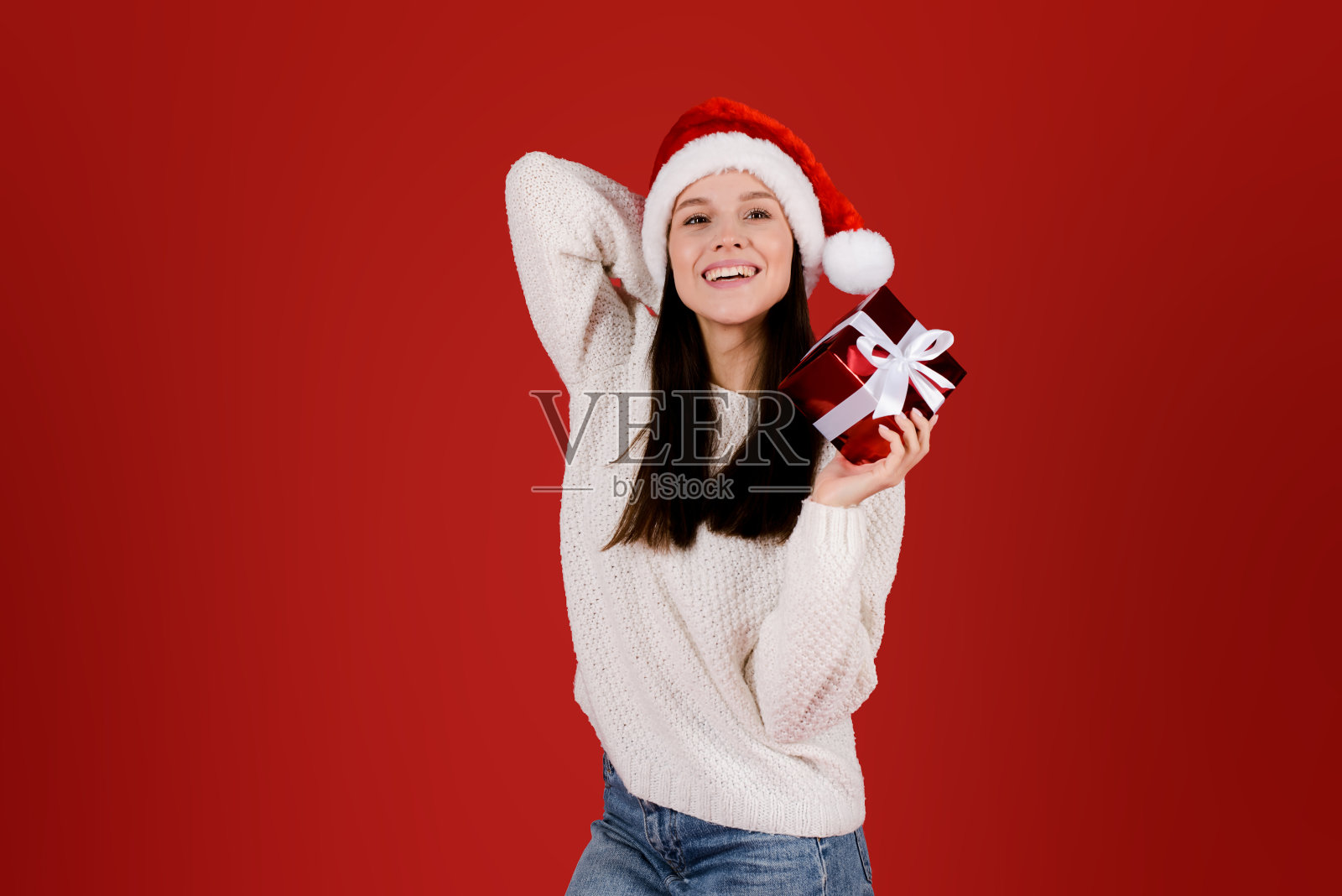 兴奋年轻美丽的女人穿着白色毛衣拿着圣诞礼物盒，孤立在红色的背景照片摄影图片