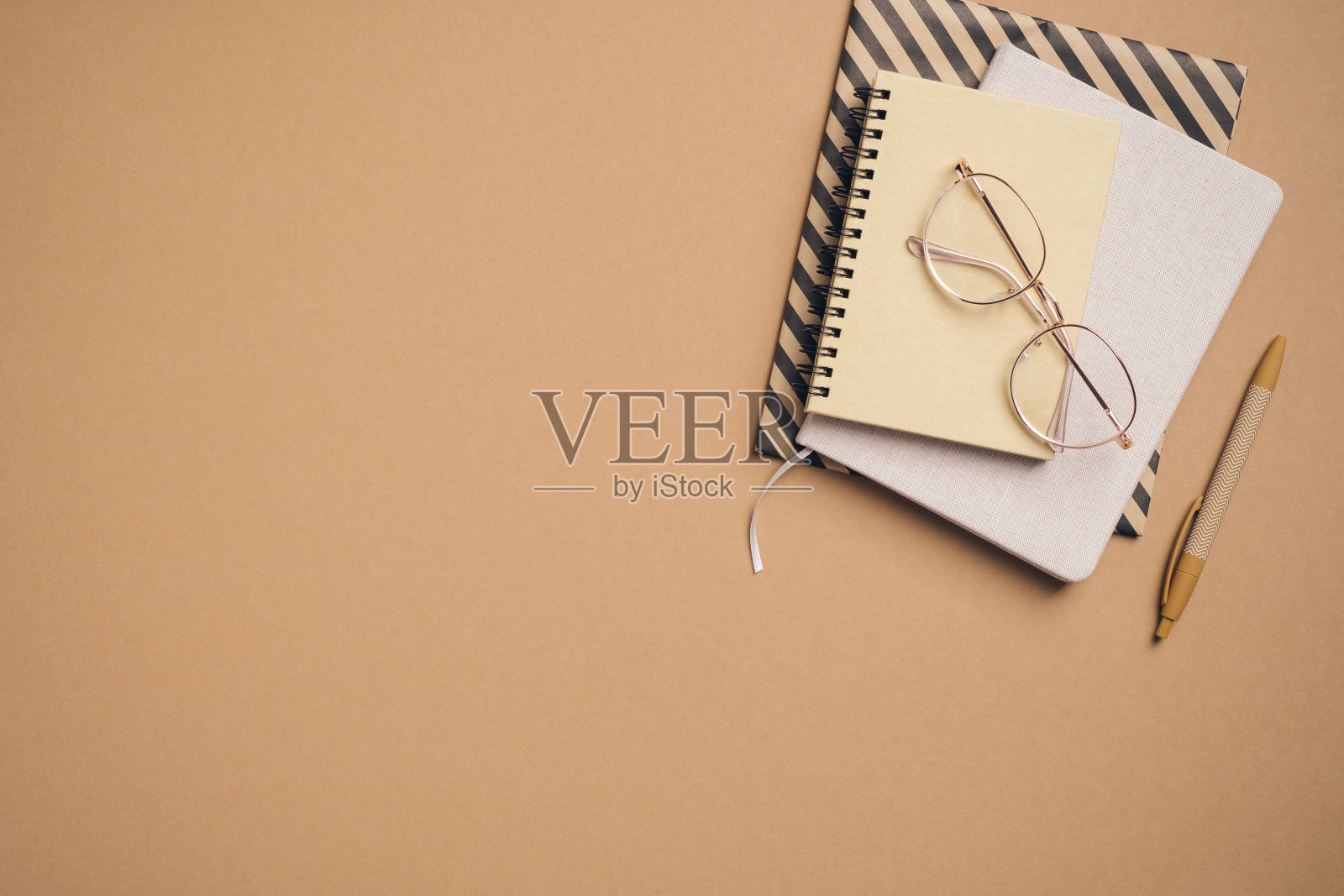 纸笔记本，记事本和女性眼镜在柔和的棕色背景。日记的概念。平躺，俯视图。照片摄影图片