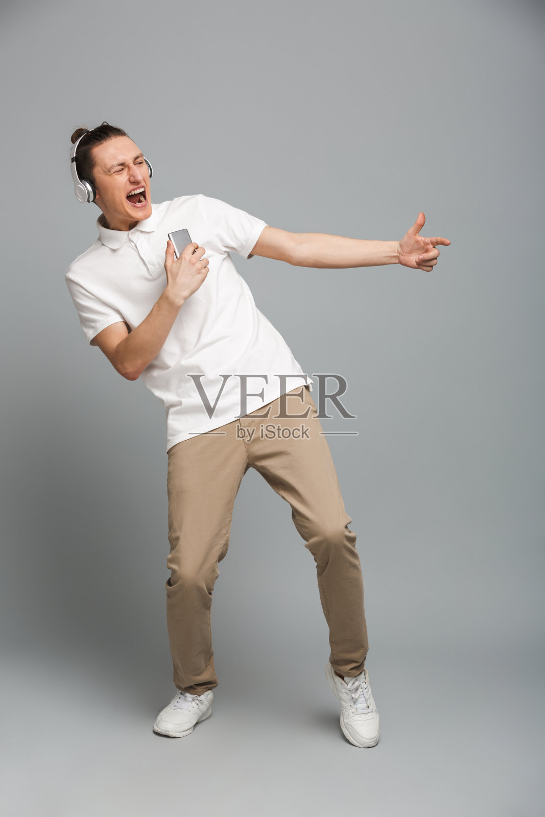 兴奋的年轻人拿着手机戴着耳机听音乐。照片摄影图片