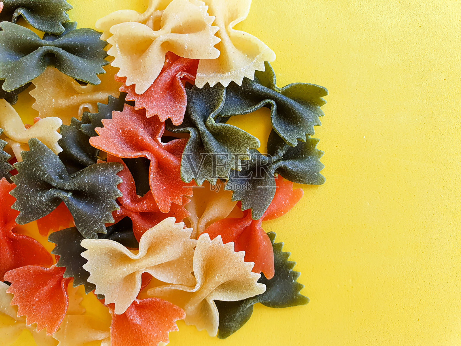 黄色背景上的意大利面图案。从上面看，各种颜色的蝴蝶结、蝴蝶结和意大利面。前视图。照片摄影图片
