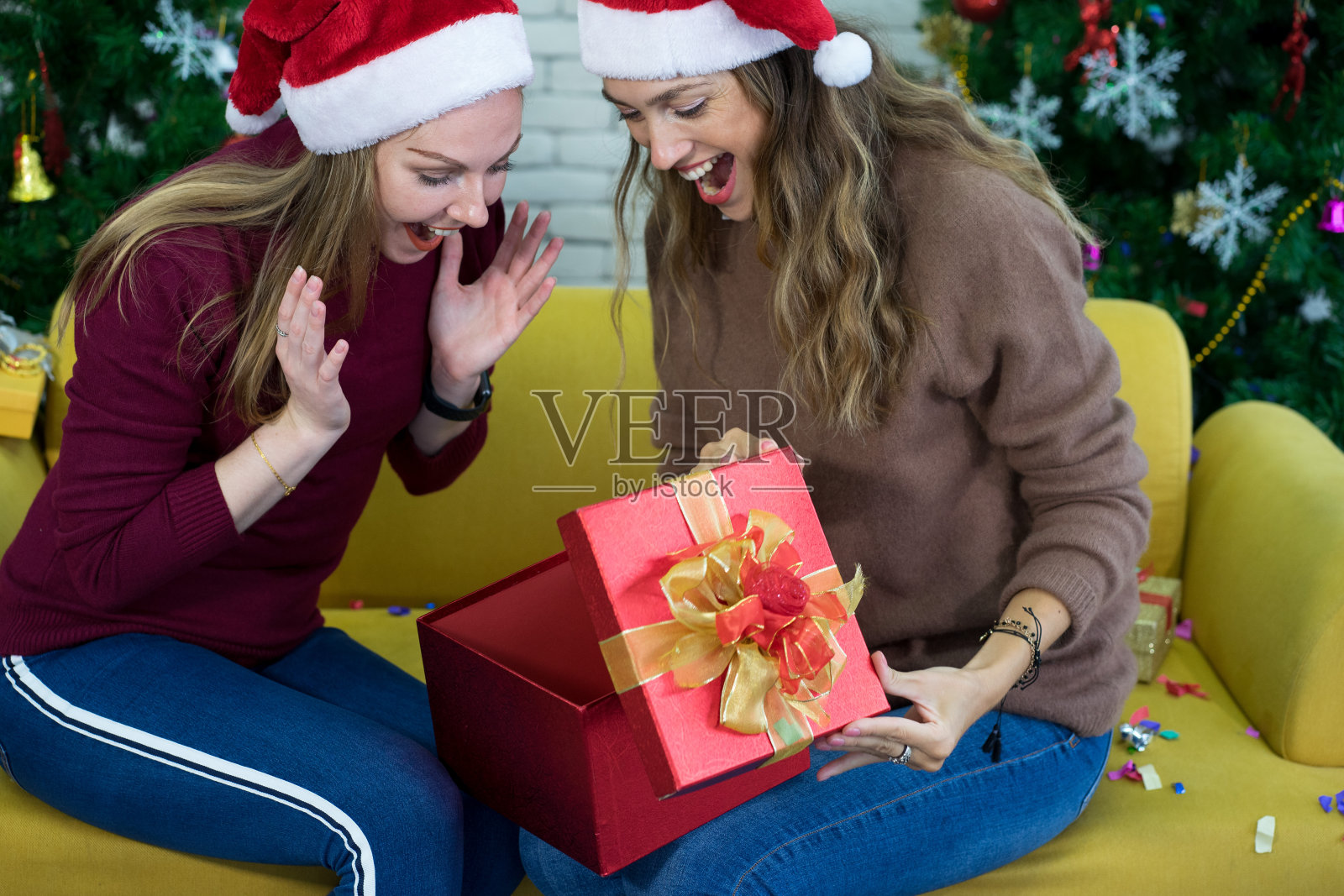 白种妇女在圣诞节聚会在黄色的沙发和圣诞树上交换礼物照片摄影图片