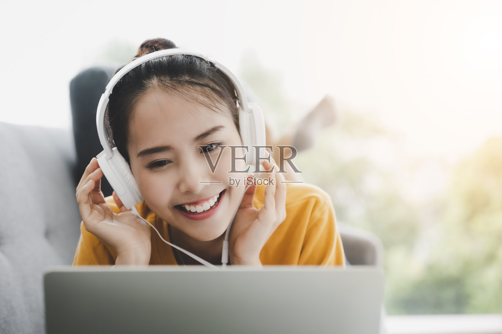 美丽的年轻亚洲女子使用笔记本电脑和戴着耳机听音乐，躺在客厅的沙发上照片摄影图片