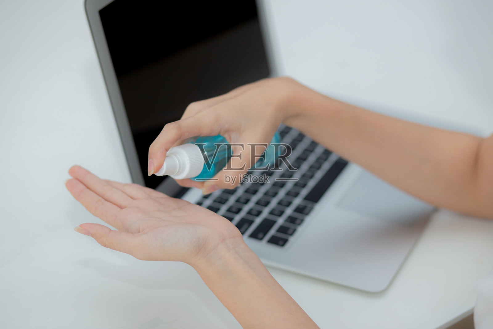 在家工作的女性用酒精凝胶或洗手液洗手并保护冠状病毒或新冠病毒，新常态，隔离和社交距离，使用笔记本电脑的商业女性。照片摄影图片