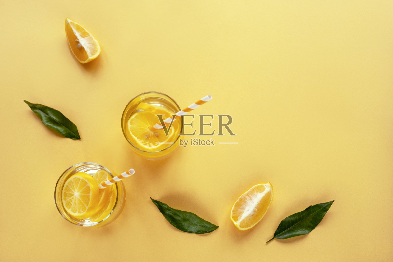 一片柠檬和绿叶在黄色的背景和两杯柠檬水。俯视图，平放，复制空间。照片摄影图片