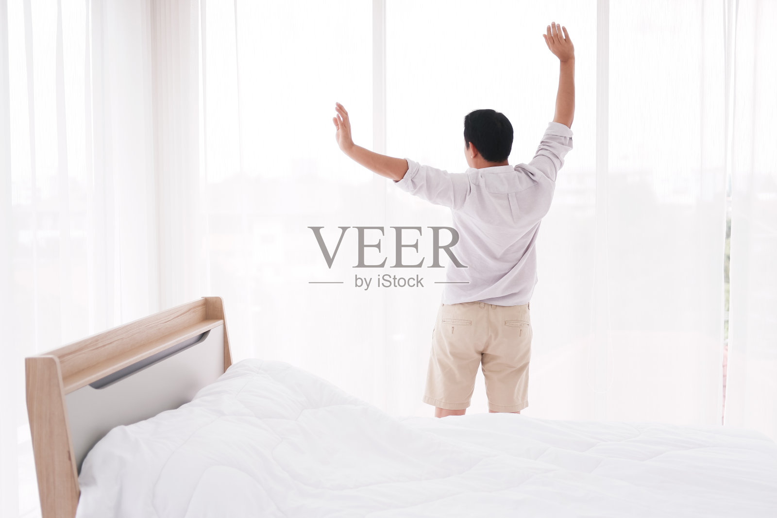 一名亚洲男子在卧室醒来后正在懒洋洋地伸懒腰。小睡之后他觉得神清气爽。照片摄影图片