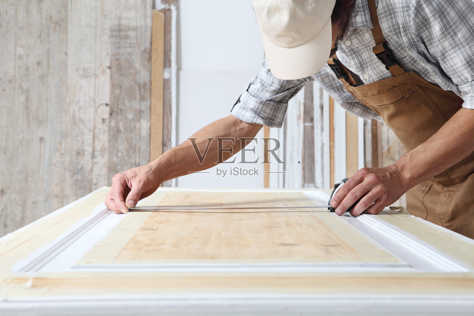 男木匠在木工车间工作，用卷尺量木门，穿戴工作服和帽子照片摄影图片