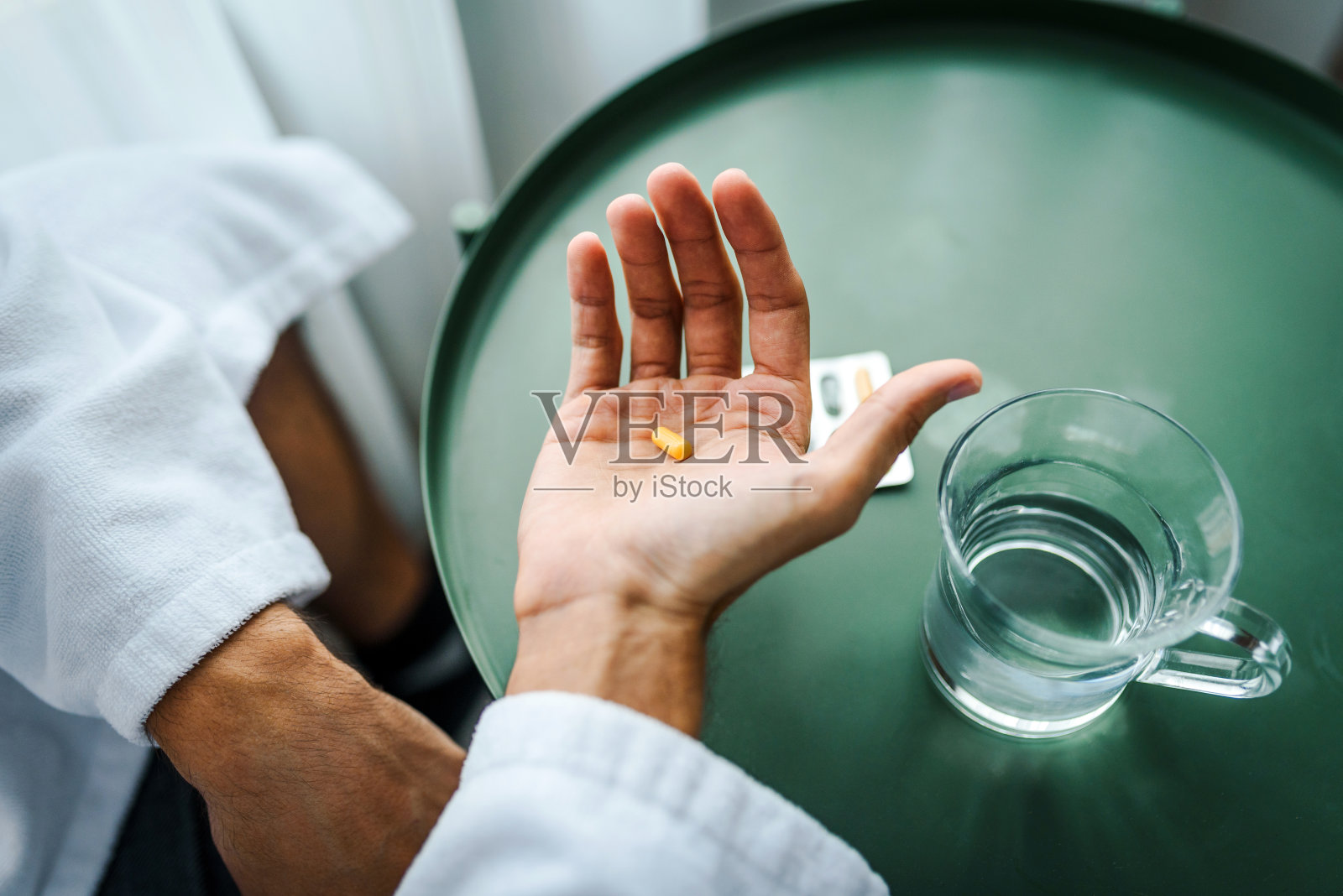 男子手中拿着药丸，桌上有杯水，药物治疗概念照片摄影图片