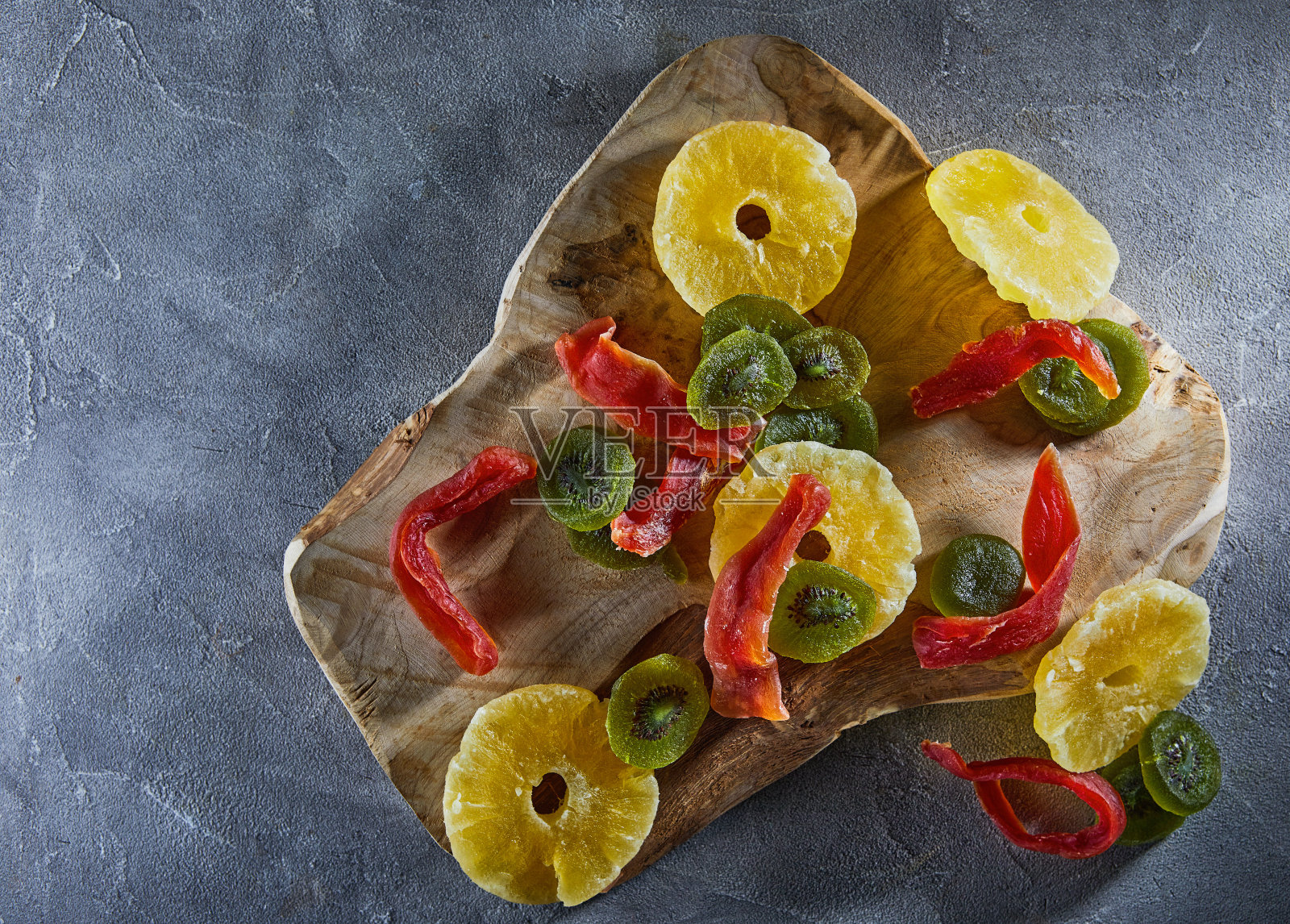 干果：灰色混凝土木砧板上的黄色蜜饯菠萝圈、红色木瓜和绿色猕猴桃照片摄影图片
