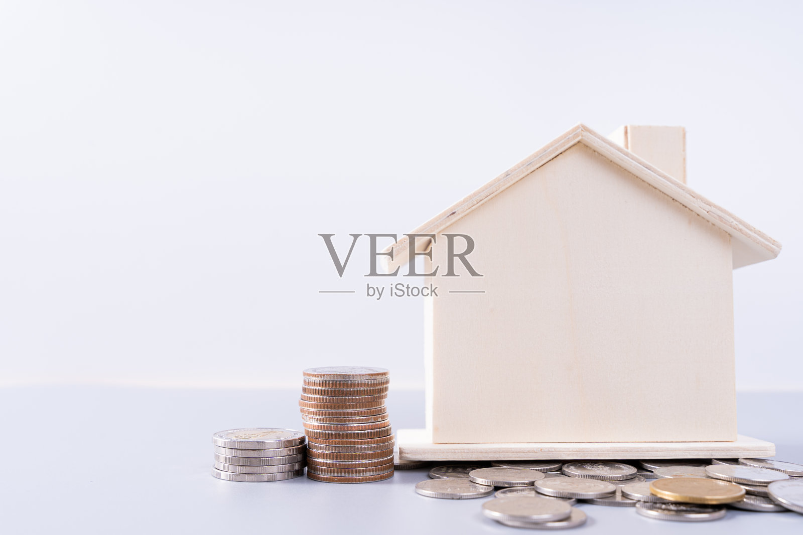 木房子与堆叠硬币孤立的灰色背景。物业投资和房屋抵押的金融概念。照片摄影图片