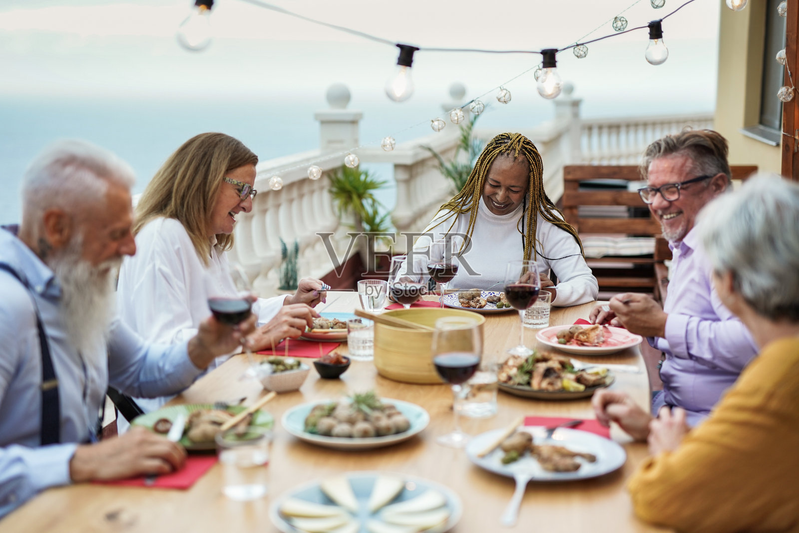 快乐的多种族高级朋友享受晚餐在家里的露台-食物和饮料照片摄影图片